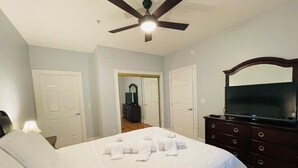 A hotel room with a bed, a ceiling fan, a dresser with a TV, and a door leading to another room. - First floor gorgeous condo in Myrtle Beach (Myrtle Beach)