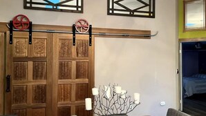 Una habitación con puerta de madera, una mesa de comedor con un centro de mesa de velas y dos adornos en las paredes.