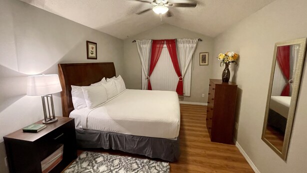 A bedroom with a bed, a bedside table with a lamp, a dresser, a ceiling fan, and a mirror. - Blissful Guest House  (Ocoee)