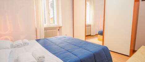Un dormitorio con cama, ventana, radiador y espejo.