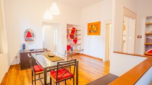 Un'area pranzo moderna con un tavolo in vetro, sedie rosse imbottite e un'opera d'arte astratta a parete.