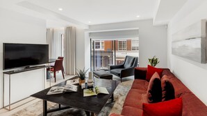 A modern living room with a flat-screen TV, a dark coffee table, a red sofa, and a black armchair.