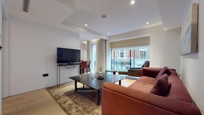 A modern living room with a flat-screen TV, a dark coffee table, a red sofa, and a large window offering a view of the city.