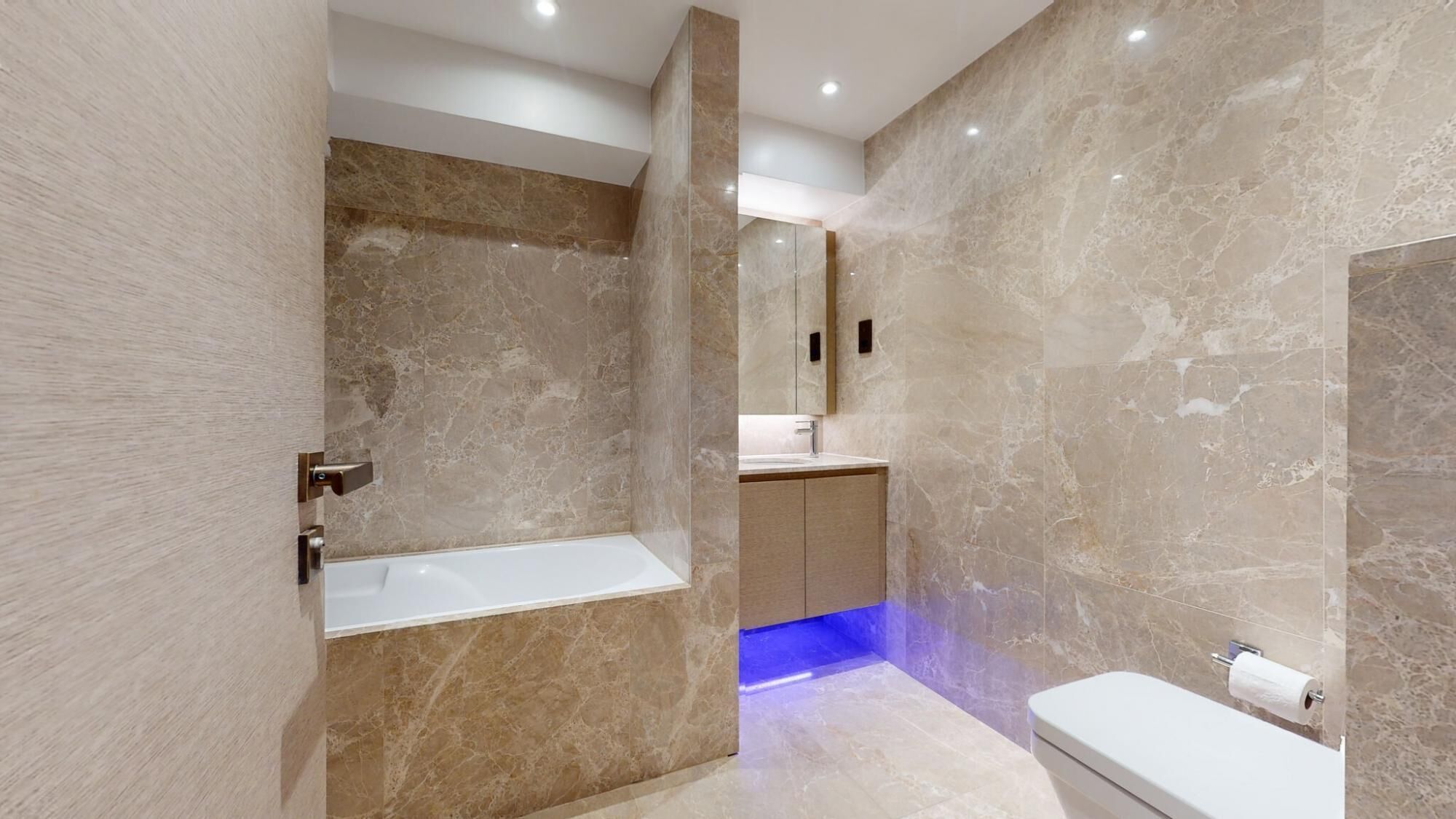 A modern bathroom with a marble wall, a bathtub, a toilet, and a sink with a mirror.