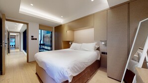 A modern hotel room with a large bed, wooden flooring, and a view of the outside.