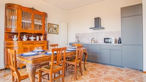 Un coin repas avec une table et des chaises en bois, une cuisine avec des placards gris, une cuisinière et un four à micro-ondes.