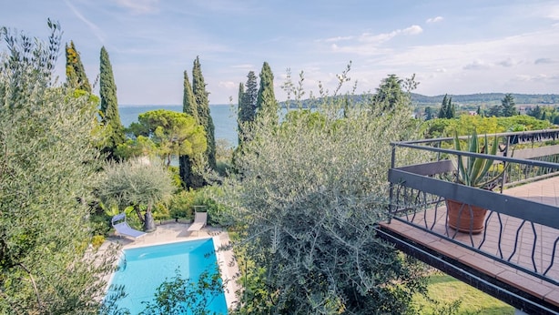 Une piscine entourée d’une végétation luxuriante et de grands arbres, avec vue sur une étendue d’eau.