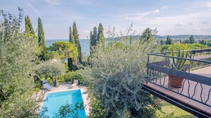 A pool surrounded by lush greenery and tall trees, overlooking a body of water. - Villa Dora - Italian Homing (Padenghe sul Garda)