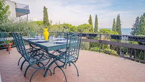 Une terrasse avec une table dressée pour le repas, offrant une vue panoramique sur des arbres et une étendue d’eau.