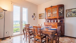 Une salle à manger avec une table en bois dressée pour six personnes, un grand buffet en bois doté de portes en verre, et une vue à travers une porte vitrée.
