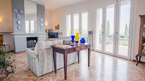 Un salon spacieux avec un grand canapé, une table basse en bois et une cheminée. De grandes fenêtres offrent une vue sur l’extérieur.