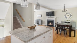 Eine moderne Küche mit Marmorarbeitsplatte, hängenden Pendelleuchten, einem Essbereich mit Holztisch und -stühlen, einer Treppe und einem Kamin.