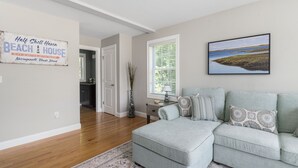 Ein Wohnzimmer mit einem hellblauen Ecksofa, einem gerahmten Bild eines Strandes und einem Schild an der Wand mit der Aufschrift "Half Shell Haven Beach House Narragansett, Rhode Island".