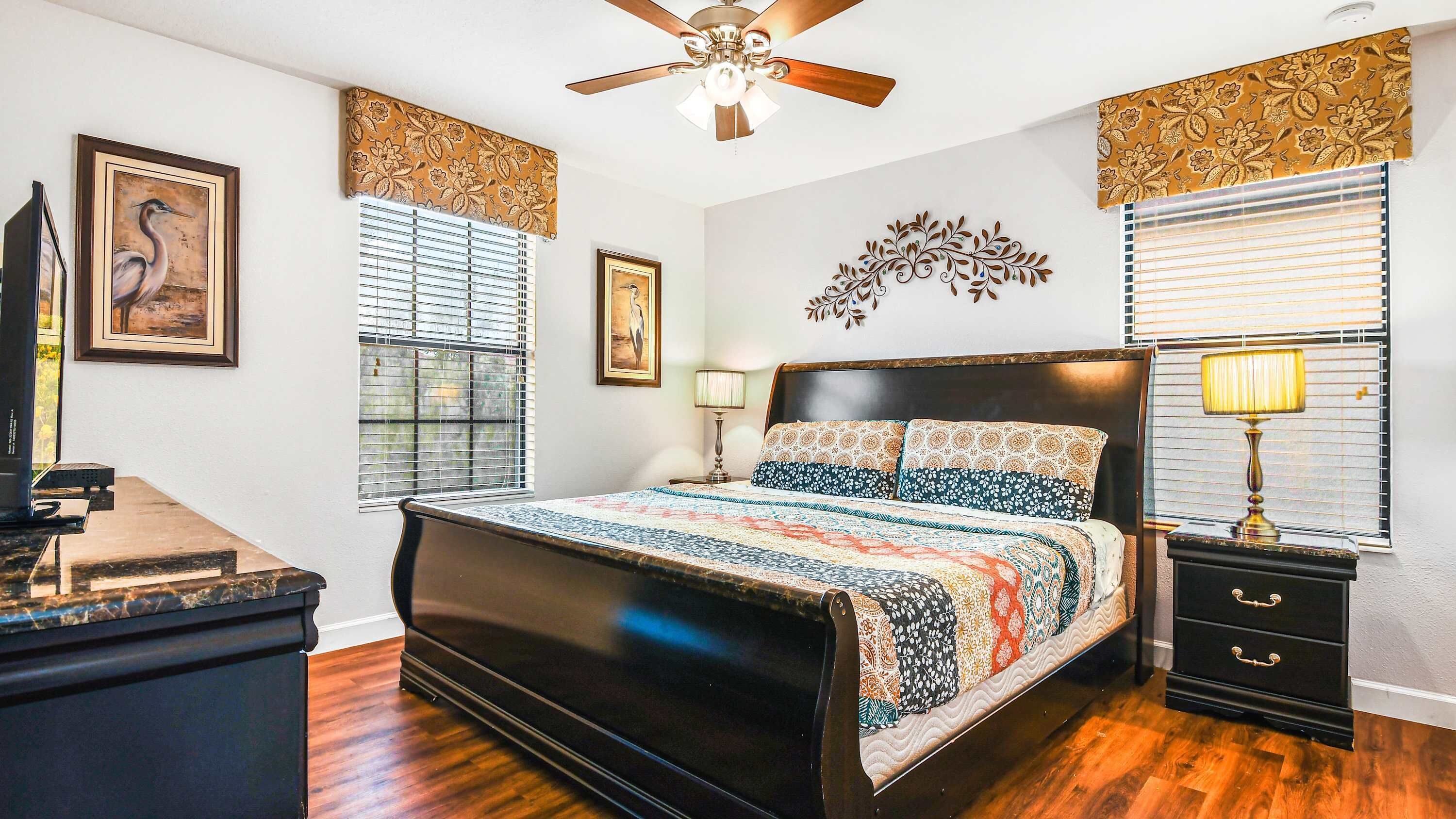 A bedroom with a bed, a desk, a ceiling fan, and decorative wall panels.