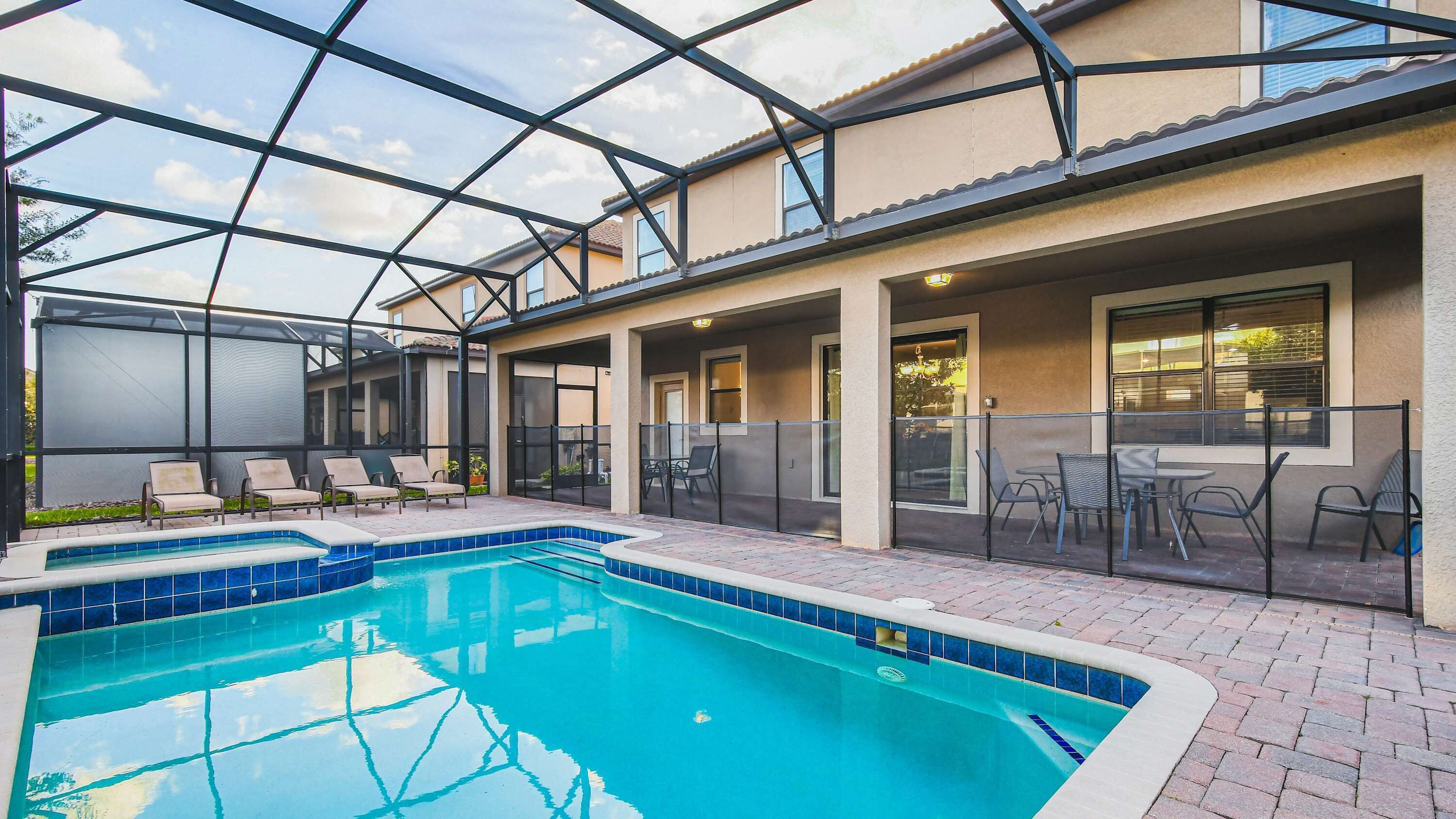 A pool area with a glass ceiling, lounge chairs, and a patio with tables and chairs.