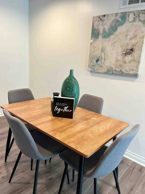 Una mesa de comedor con un cartel negro, sillas grises y un jarrón verde.