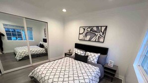 Une chambre avec un grand miroir, un lit recouvert d’une couvre-lit à motifs, une table de chevet avec une lampe et une œuvre d’art murale.