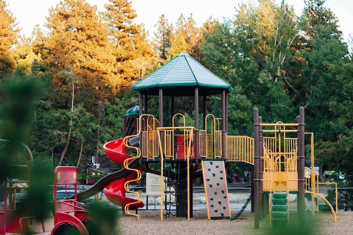 Leikkikentällä on viherkattoinen huvimaja, punainen liukumäki ja erilaisia kiipeilyrakenteita.