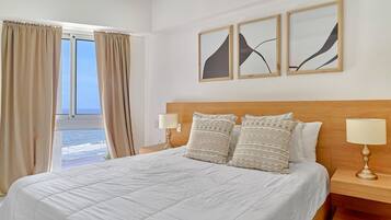 A hotel room with a large bed, two bedside lamps, a wooden headboard, and three abstract paintings on the wall.