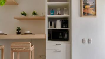 Cocina moderna con armarios blancos, microondas y cafetera. Hay dos taburetes de madera y una pequeña planta en maceta sobre la encimera.