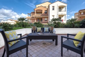 A patio with a table and chairs, surrounded by plants and a building in the background.