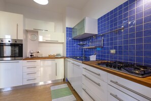 A modern kitchen with white cabinets, a stainless steel oven, a gas stove, and blue tiled backsplash.