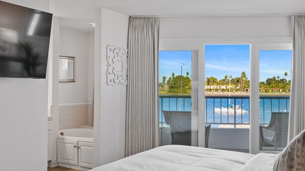 Een hotelkamer met een bed, een badkamer en een balkon met uitzicht op het zwembad.