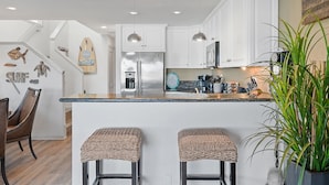 Een moderne keuken met witte kasten, roestvrijstalen apparatuur en een centraal eiland met barstoelen.
