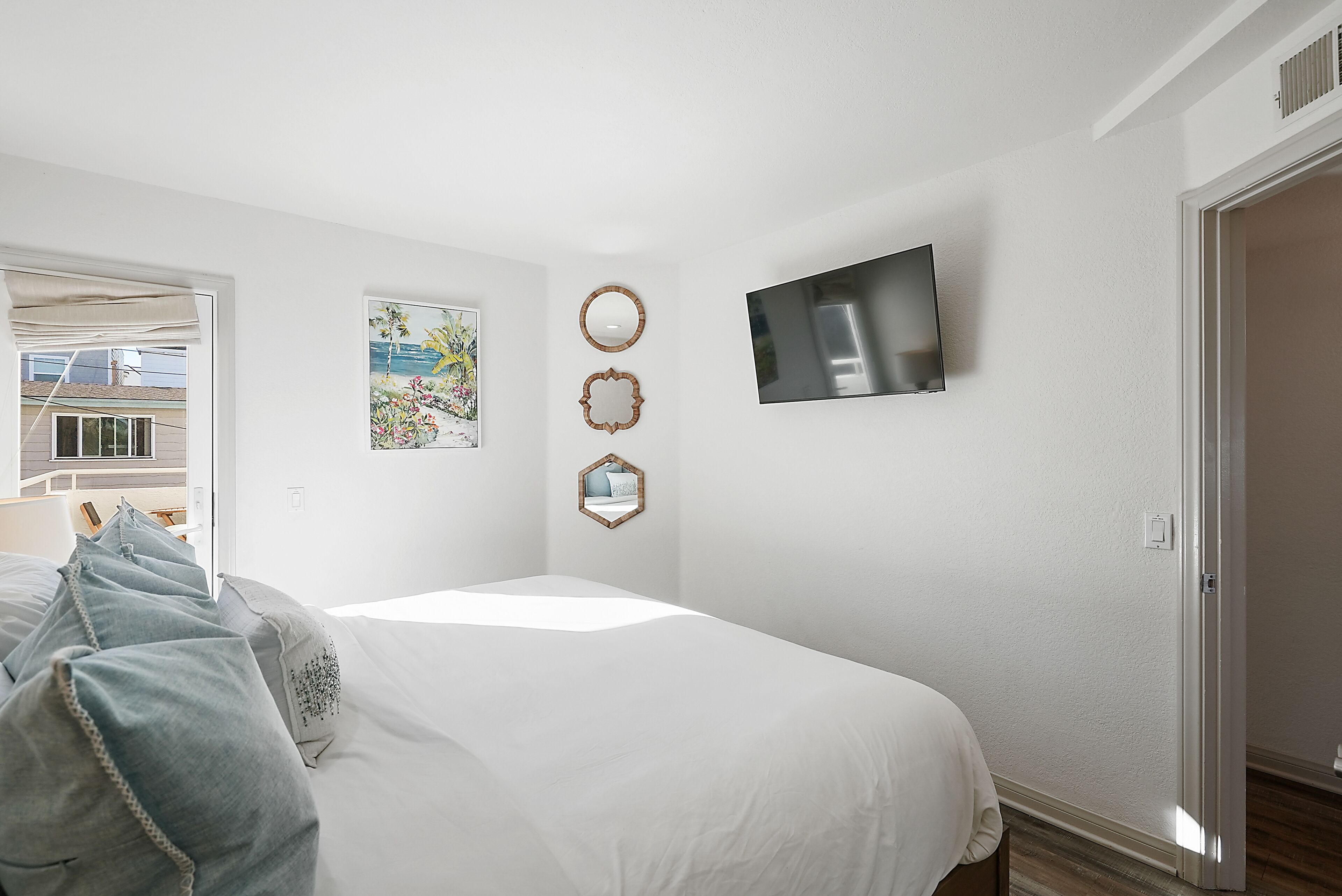 A bedroom with a bed, a TV mounted on the wall, and a door leading to another room.