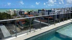 A modern building with a pool, a view of the ocean, and a clear sky. - Bela Hospedagem - Lindo flat no Box 150 (João Pessoa)