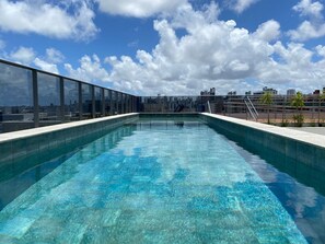 A rooftop pool with clear blue water, surrounded by a glass railing, overlooking a cityscape. - Bela Hospedagem - Lindo flat no Box 150 (João Pessoa)