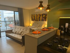 A modern hotel room with a sofa, dining table, and kitchen area. - Bela Hospedagem - Lindo flat no Box 150 (João Pessoa)