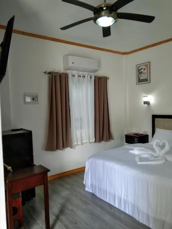 A hotel room with a bed, a ceiling fan, an air conditioner, a desk, and a nightstand. - Tequila Cove (Panglao)