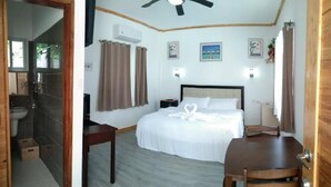 A bedroom with a bed, bedside tables, a desk, and a chair. There is a shower area visible through an open door. - Tequila Cove (Panglao)