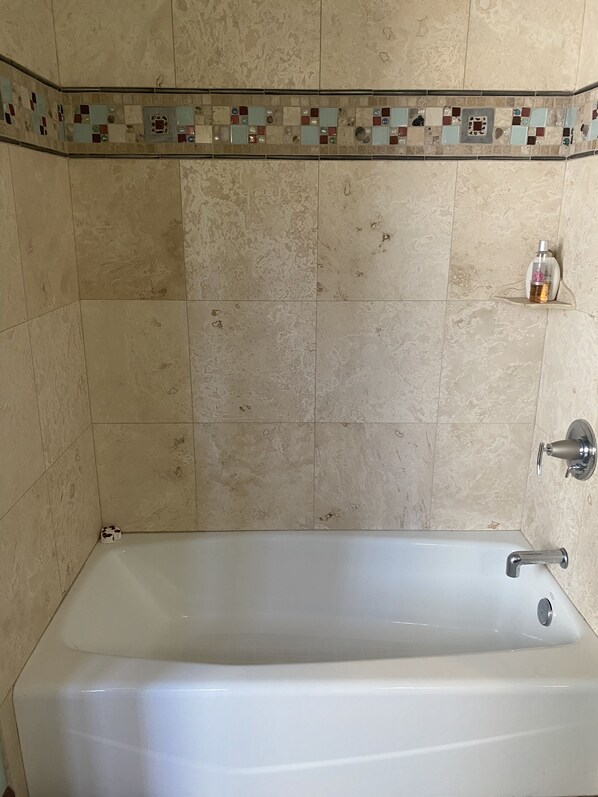 A bathroom with a bathtub, a shower, and a small shelf with a bottle.