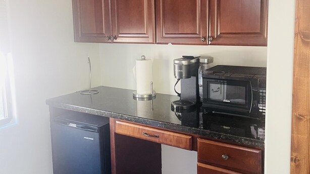 Una cocina compacta con armarios de madera, una encimera negra, lavavajillas, cafetera y microondas.