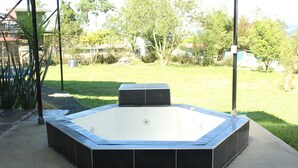 Een jacuzzi met een zwart betegelde buitenkant, omringd door een betonnen terras, gelegen in een achtertuin met gras en bomen.