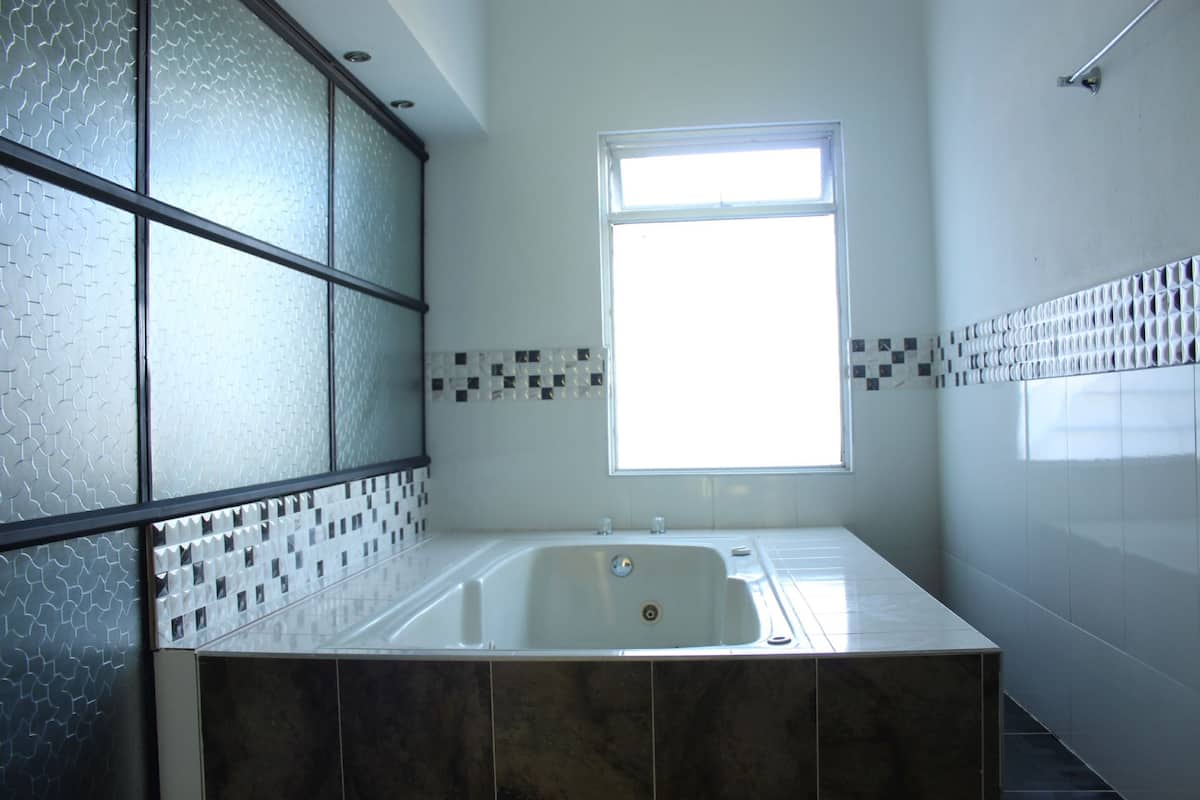 Une salle de bain dotée d’une grande baignoire, de panneaux en verre dépoli et d’une fenêtre laissant entrer la lumière naturelle.