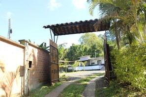 A gated entrance with a metal gate, a brick wall, and a pathway leading to a building with a tiled roof. - VILLA NATALIA (Santa Rosa de Cabal)