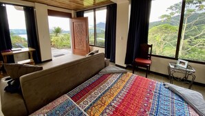 Ein Schlafzimmer mit einem großen Bett, Holzbalkendecke, Blick ins Freie, einem Schreibtisch und einem Stuhl.