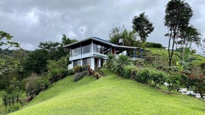 Ein modernes Haus mit Flachdach und großen Fenstern, umgeben von üppiger Vegetation und einer sanften Hanglage.