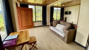 Ein geräumiger Wohnbereich mit Holzbalkendecke, einer Couch, einem an der Wand befestigten Fernseher und einem Tisch mit einem Laptop.