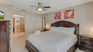 A bedroom with a large bed, a ceiling fan, a wooden dresser, and a door leading to a bathroom. - Fully Fenced, Extra Large Lot, Private Pool & Spa Close to Attractions, Restaurants & Supermarkets (PG2200) (Clermont)