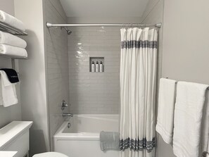 Un baño con ducha, bañera y retrete. Hay toallas colgadas en un perchero y una repisa.