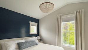 A bedroom with a large bed, a window with curtains, a bedside table with a lamp, and a hanging light fixture. - Cozy Cottage in Seabrook w/ Private Hot Tub (Pacific Beach)