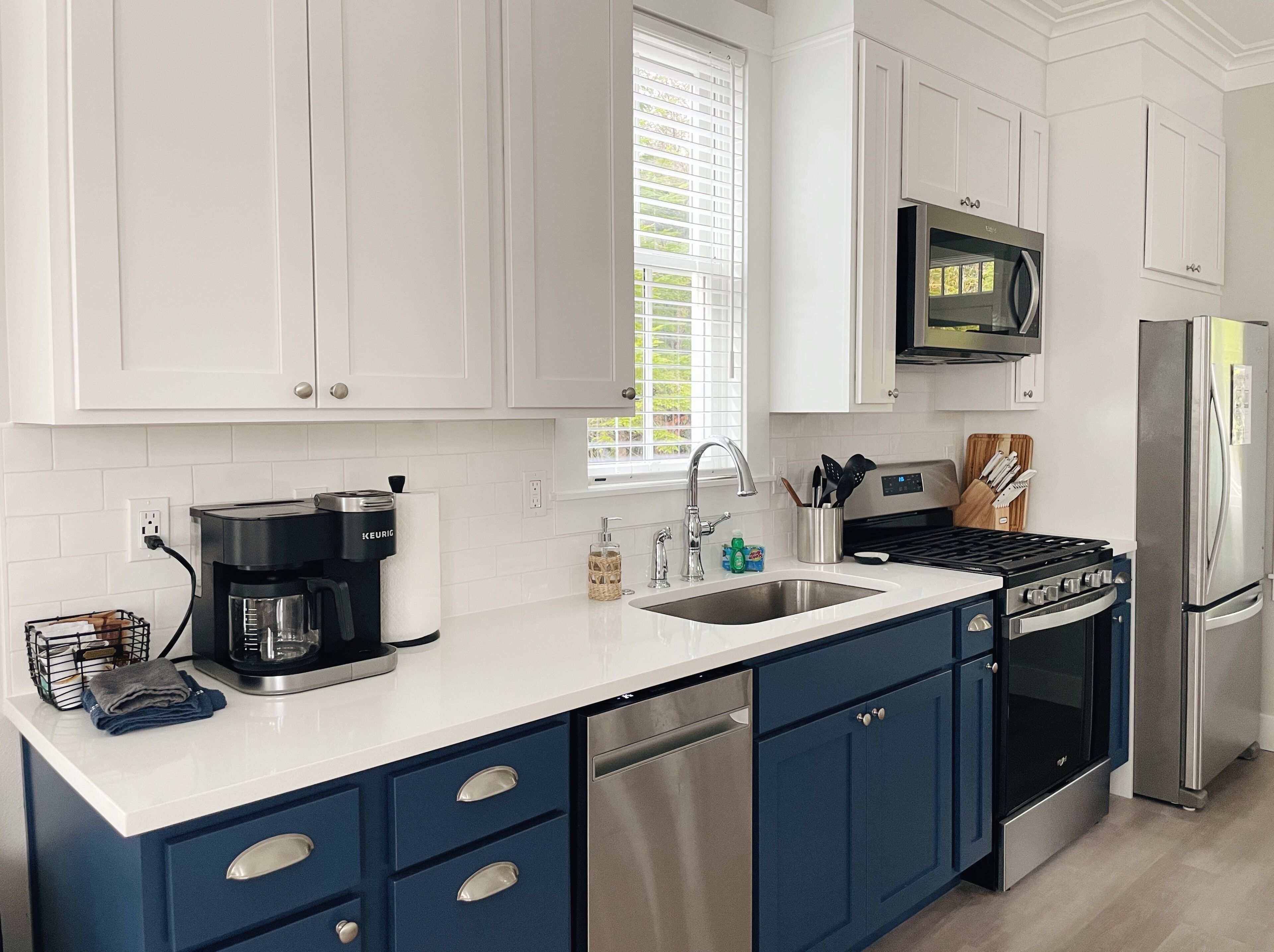 A modern kitchen with white cabinets, a black stove, stainless steel appliances, and a window with blinds.