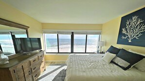 A bedroom with a large bed, a TV on a wooden dresser, and a view of the beach through large windows. - The fish are biting!!🎣🌞 There is something for everyone! (Orange Beach)