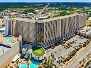 A large hotel with multiple floors, a swimming pool, and a parking lot.