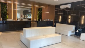 A modern reception area with a black marble reception desk, white sofas, and a vertical garden. - Vila do Centro Apart Hotel (Bombinhas)