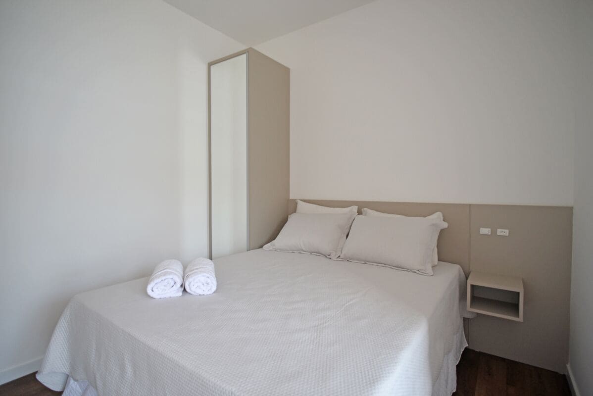 A minimalist hotel room with a large bed, two pillows, a nightstand, and a mirror.